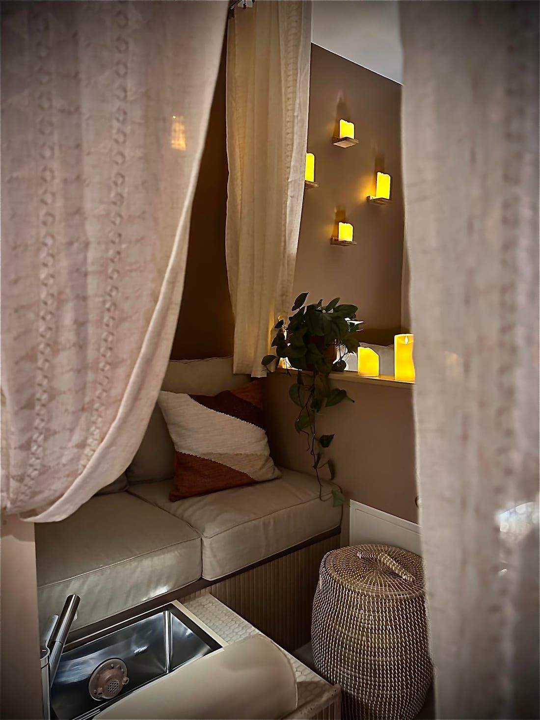 The curtained pedicure nook at Alora Wellness Spa in Pittsburgh, with a candlelit wall, a cushioned bench and a foot basin