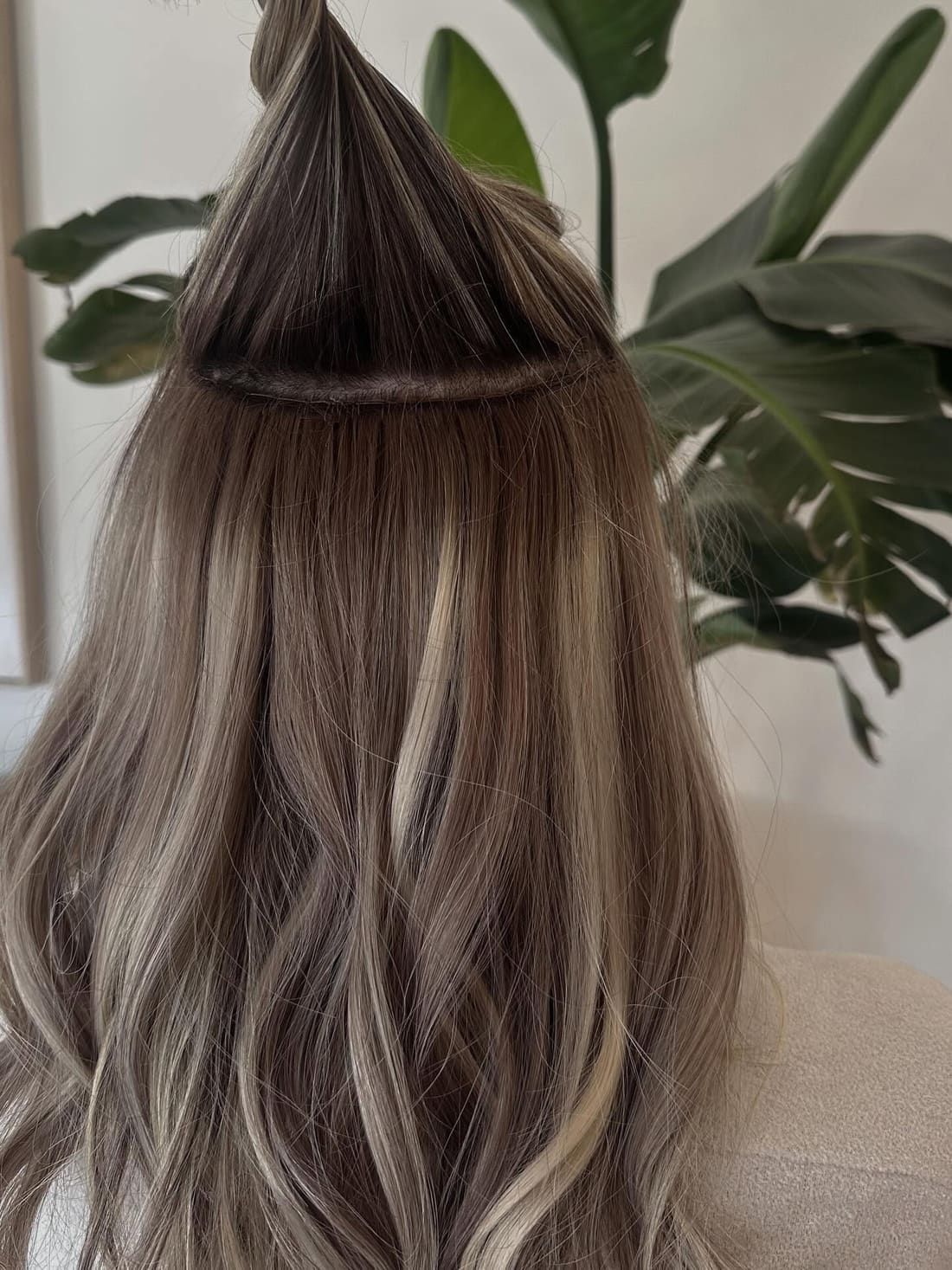 A hand-tied weft extension row fitted close to the root under a section of ash brown hair at Alora Salon in Pittsburgh